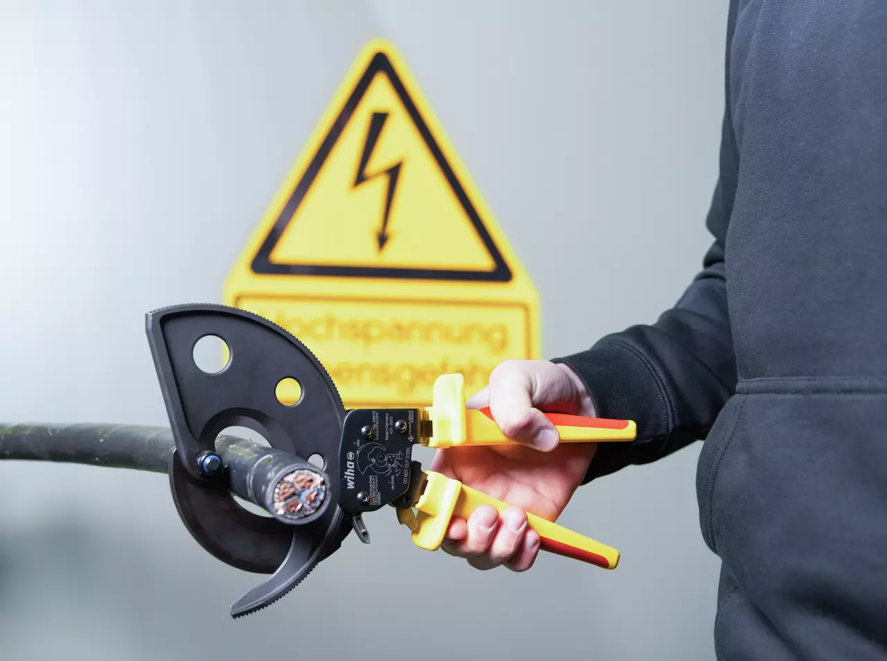 Pince coupe-câbles isolée Wiha 46675 sur un câble multibrins, en environnement électrique signalé par un panneau de danger