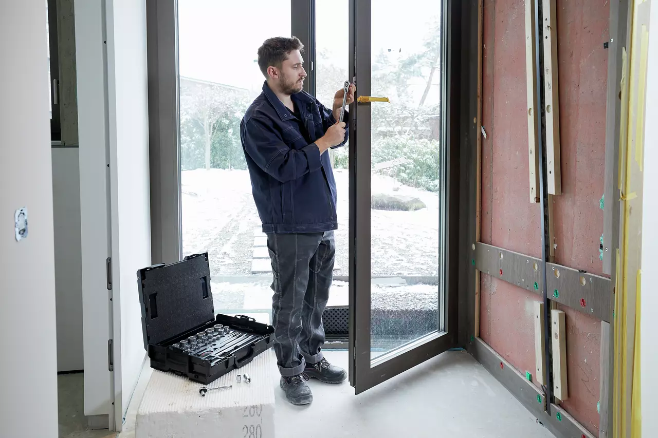 Coffret Wiha 44685 posé au sol sur un chantier, réglage d'une ferrure de porte-fenêtre au cliquet